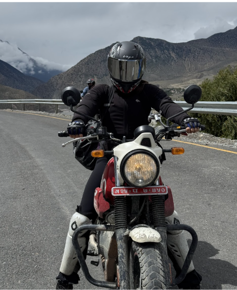 Adventure motorcyclist wearing full riding gear on a Royal Enfield scram 411 on a mountain highway in Nepal